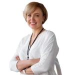 Vrouw met kort blond haar in witte blouse, armen over elkaar, voor een neutrale achtergrond