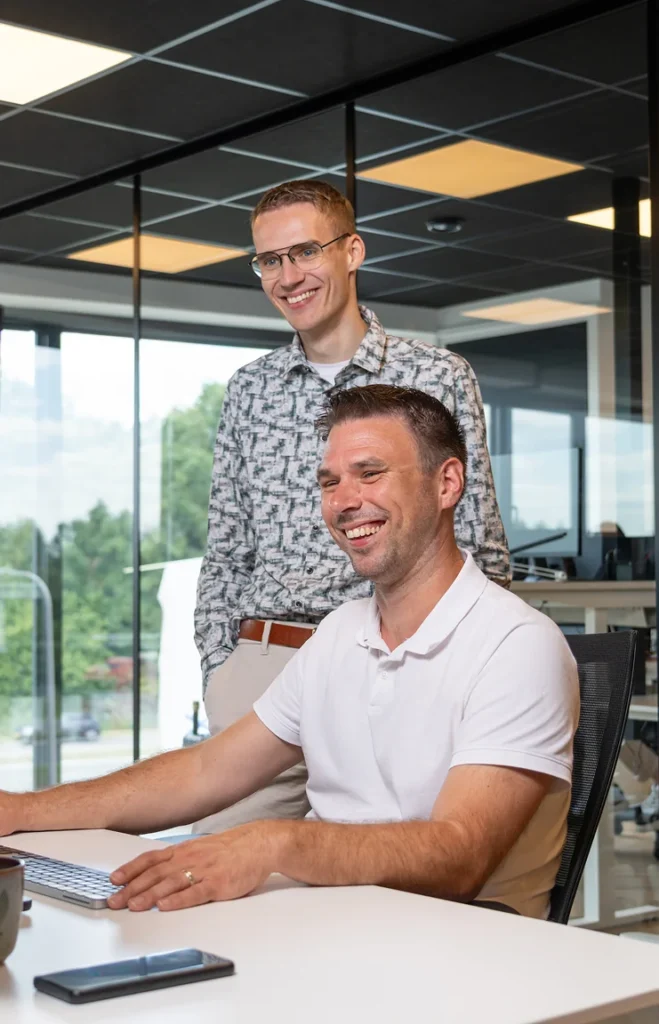 Twee collega's van Twentecs, een staand en een zittend achter een laptop