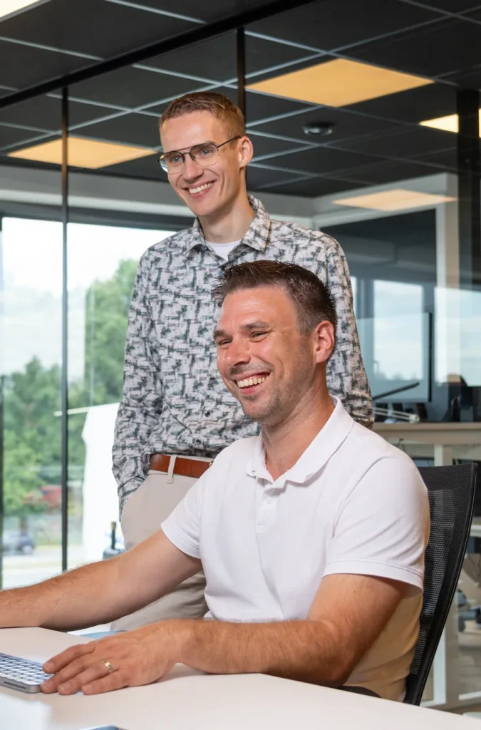 Twee collega's van Twentecs lachend achter een laptop op kantoor