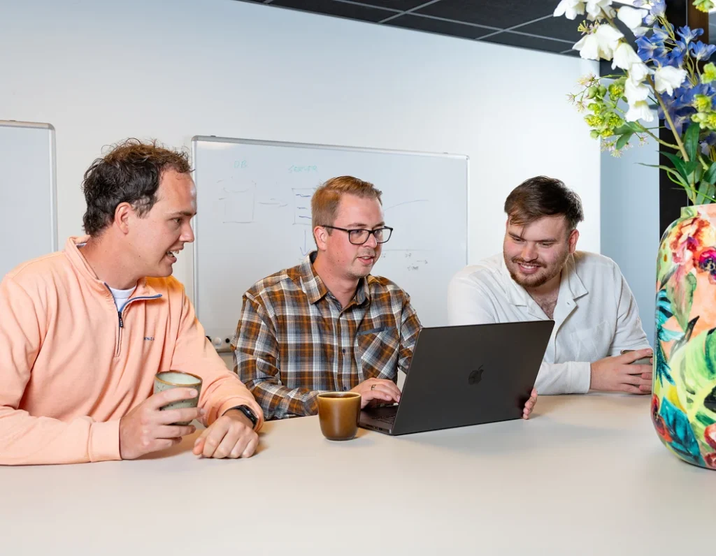 Drie collega's van Twentecs achter een laptop, met bloemen op de voorgrond