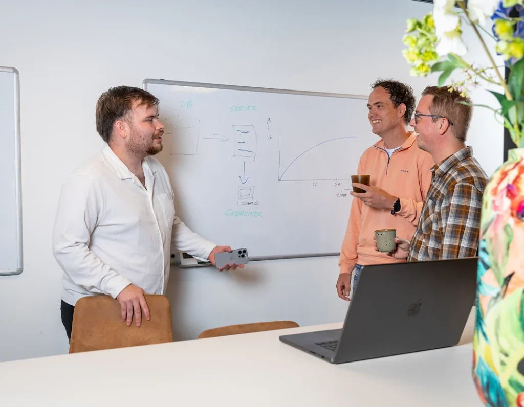 Drie collega's van Twentecs bij een whiteboard met een geschetst systeemschema tijdens een overleg.