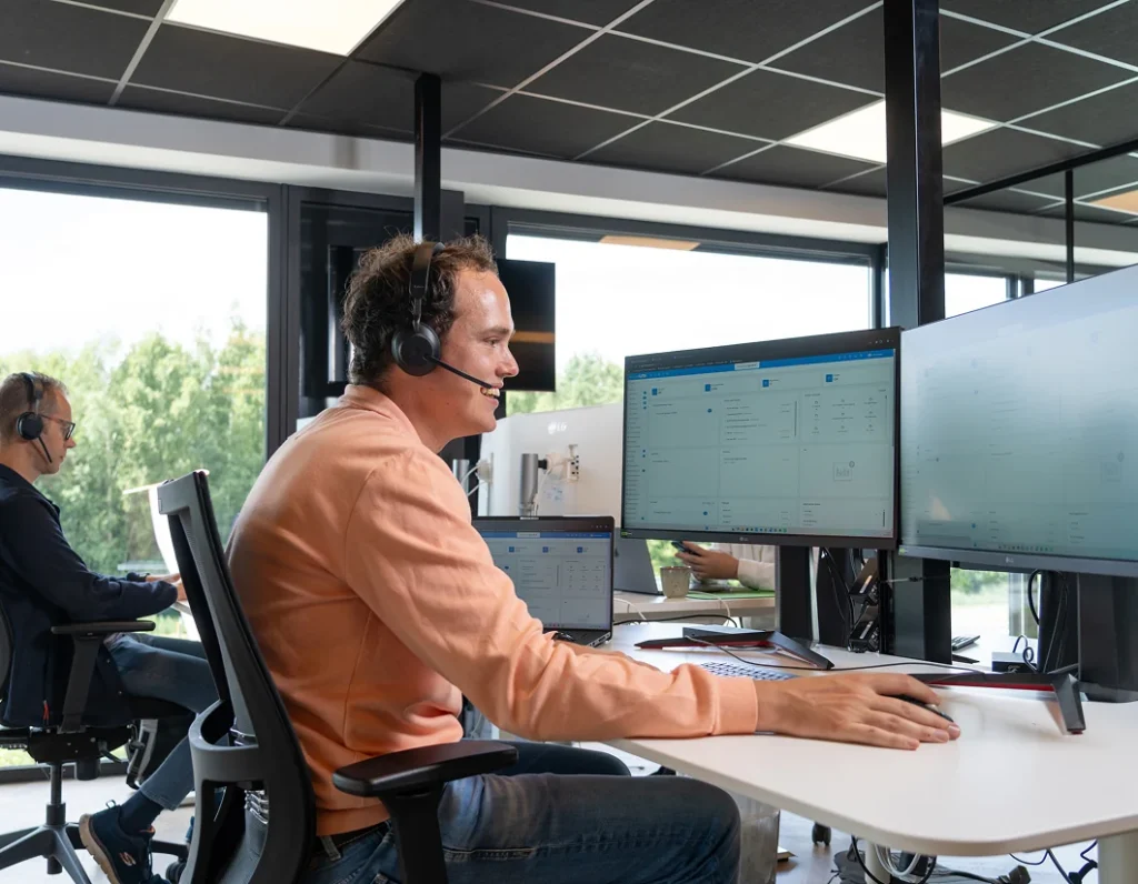 Medewerker met headset werkt aan meerdere beeldschermen op kantoor.