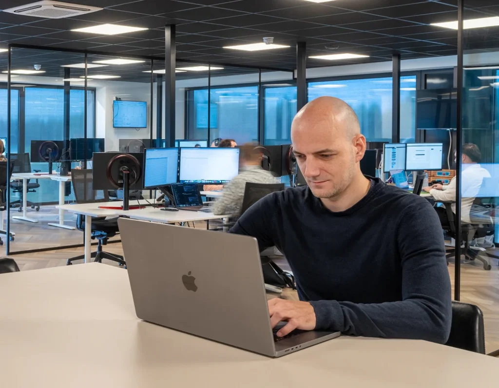 Medewerker typt op een laptop in het open kantoor van Twentecs.