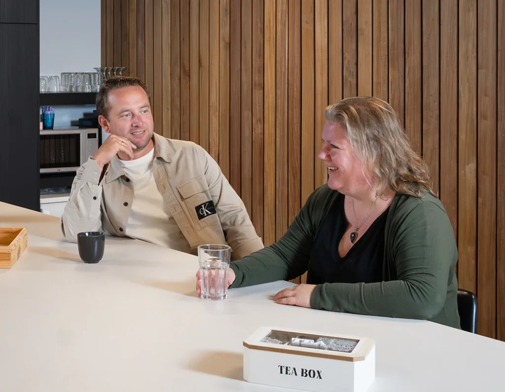 Man en vrouw van Twentecs in gesprek aan tafel met een teabox.