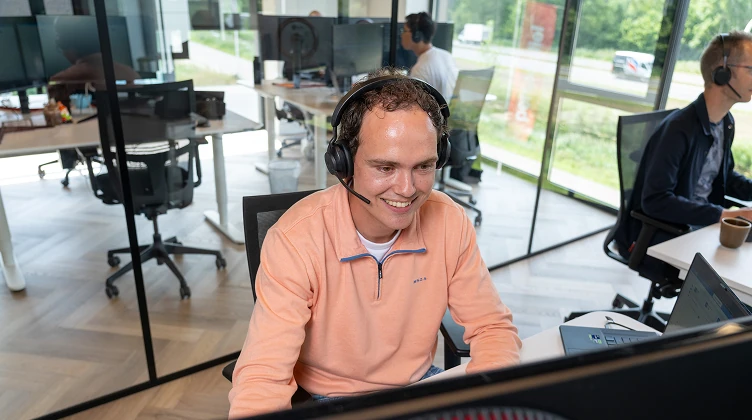 Medewerker met headset werkt achter een computerscherm.