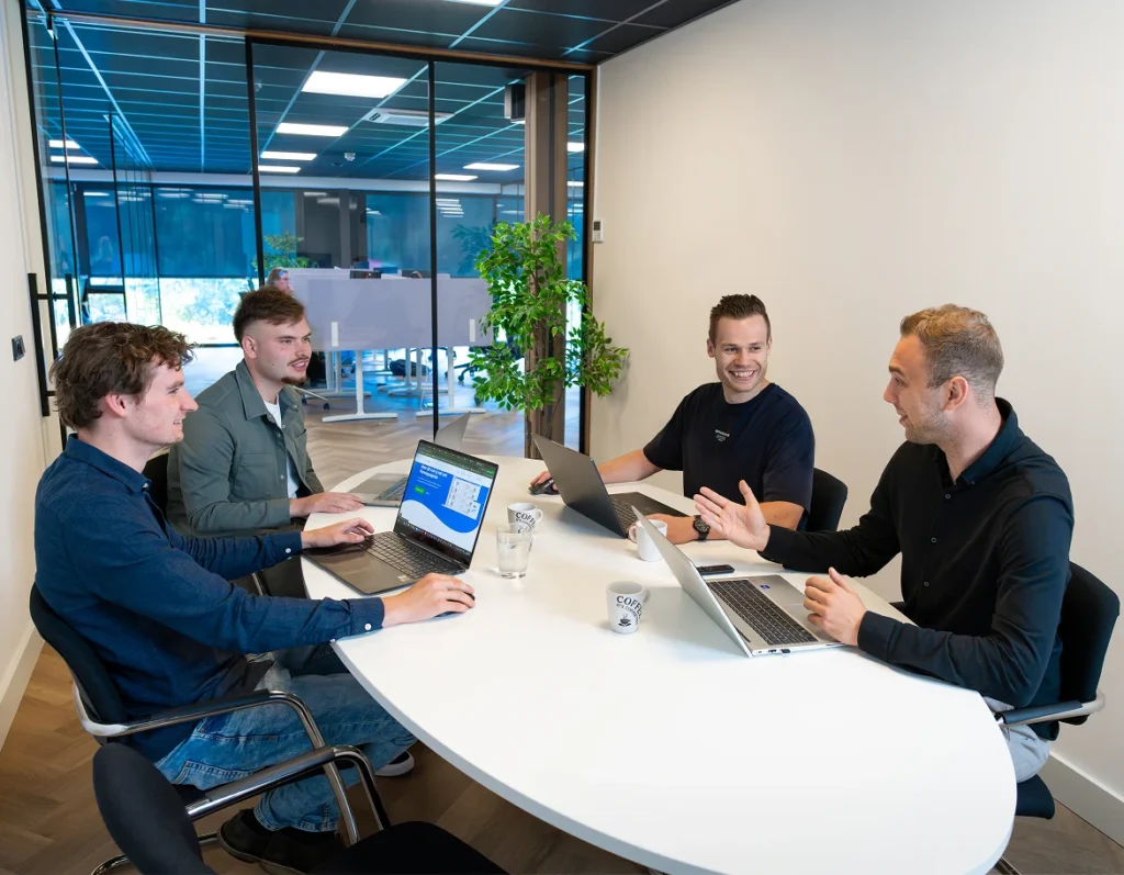 Vier collega's van Twentecs in overleg aan tafel met laptops