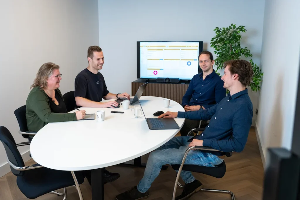 Vier collega's van Twentecs in overleg aan een tafel met een presentatie op het scherm